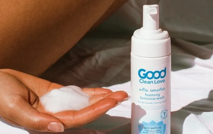 A hand holding foam next to a bottle of foaming feminine wash labeled Good Clean Love.
